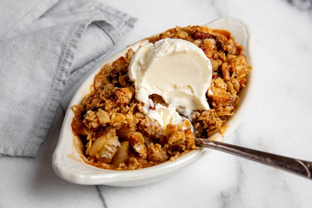 Gluten free apple crisp topped with vanilla ice cream with a spoon. 
