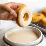 A hand dipping a donut into maple glaze.