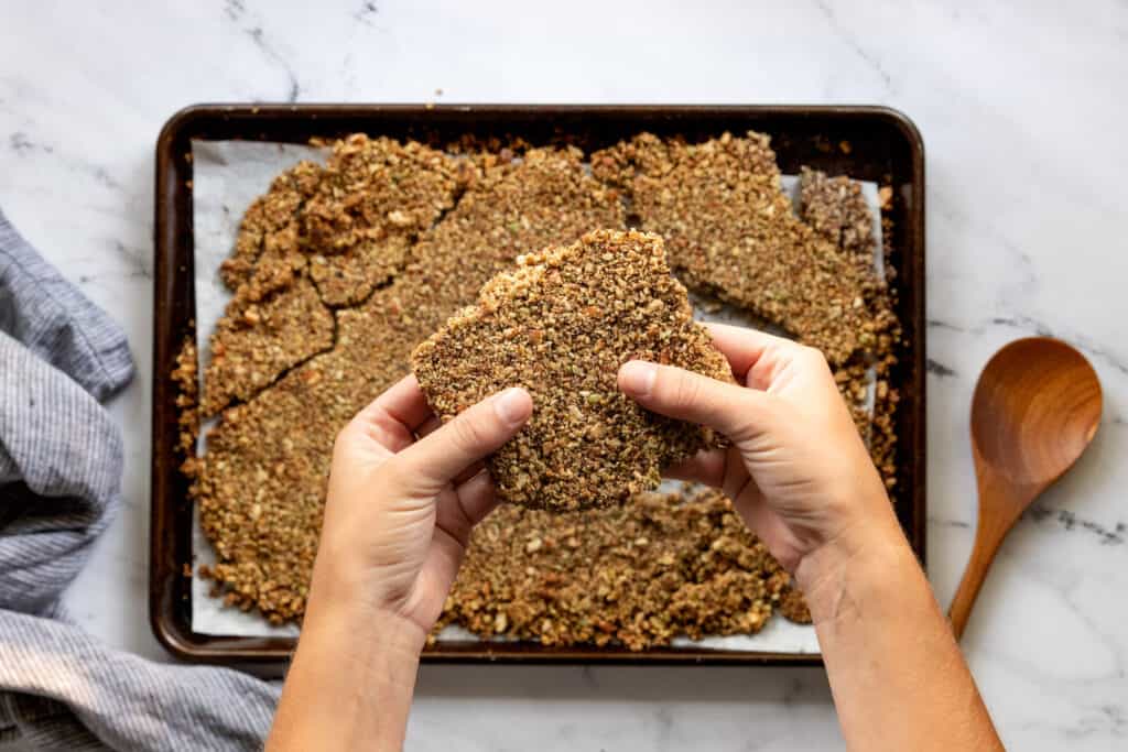 Baked granola in a baking pan with hands breaking it into clusters.