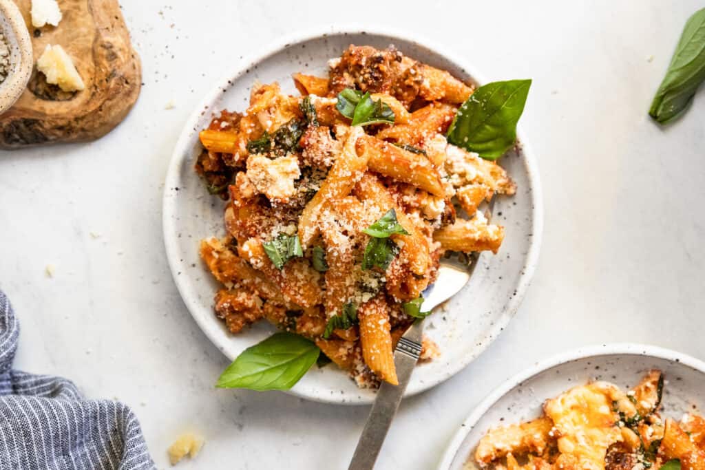 A plate of penne baked pasta with sausage, topped with parmesan and basil. 