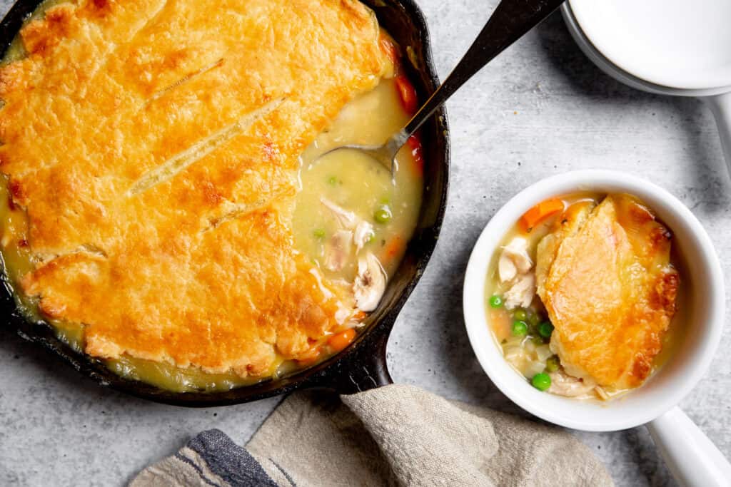 Gluten free chicken pot pie in a cast iron skillet, with a serving alongside.