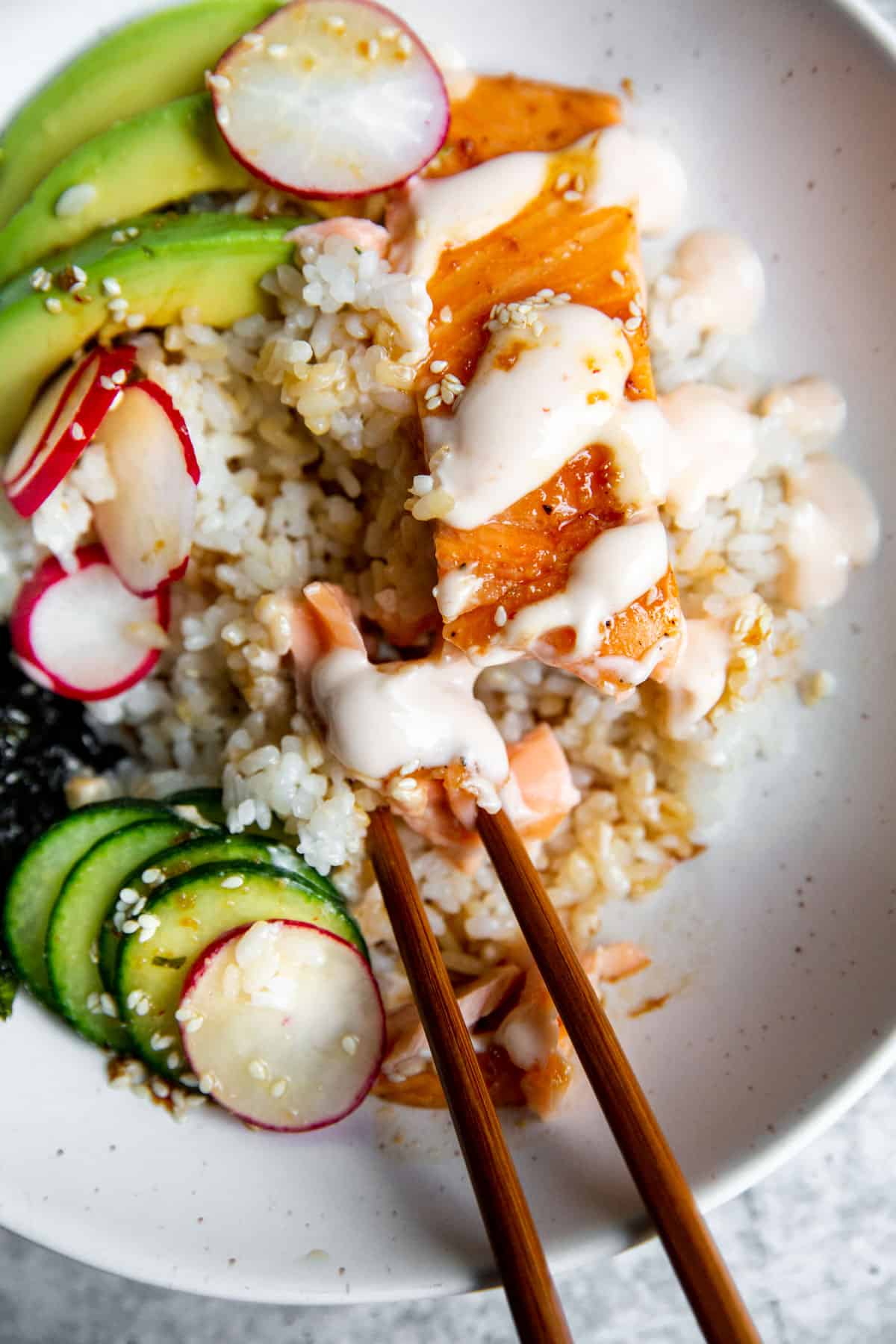 a close up shot of the contents of salmon bowls with chopsticks resting inside the bowl