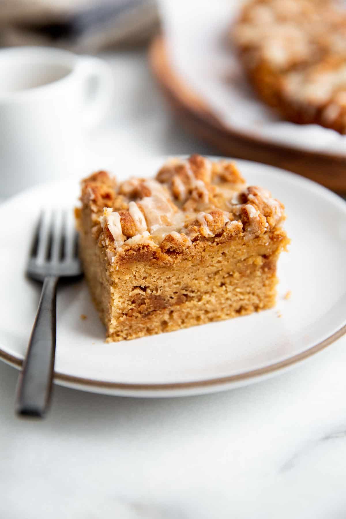 a sliced of coffee cake on a white plate with a fork next to it