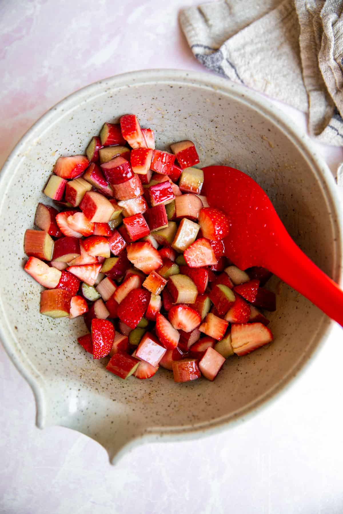 a bowl of diced strawberries and rhubarb pieces with a red spatula resting on the side