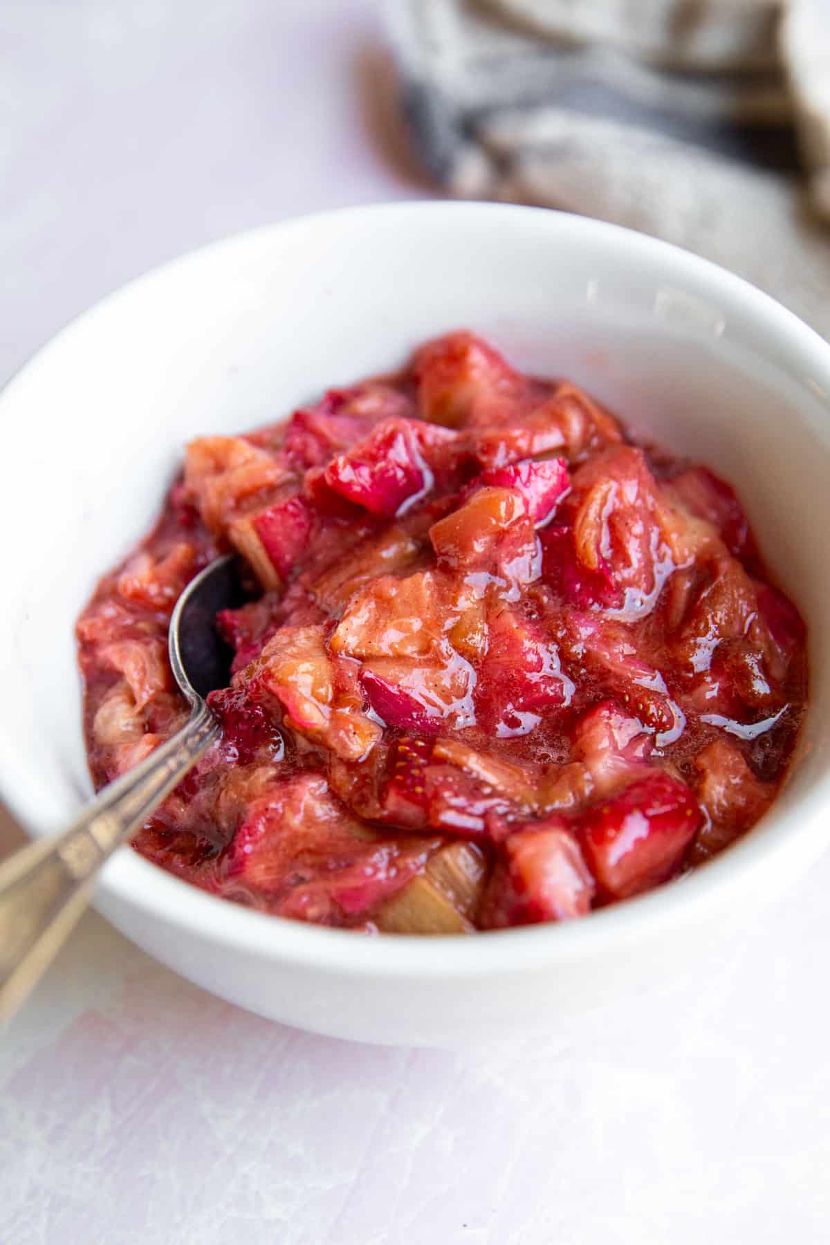 a close up photo of caramelized, roasted fruit in a white bowl with a spoon. 