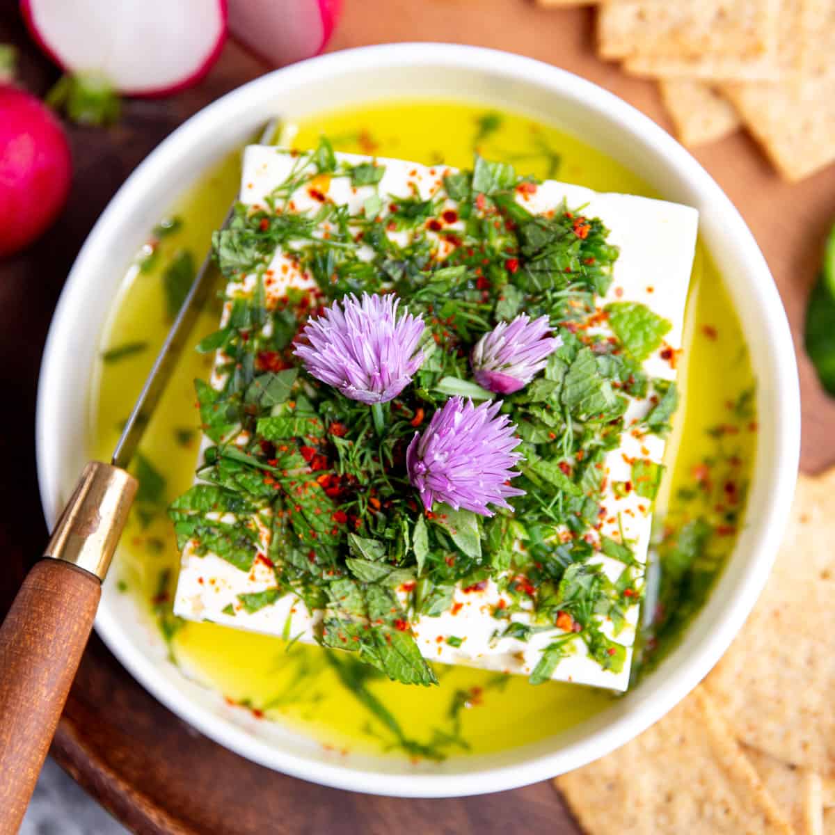 Marinated feta on a serving platter with crackers and vegetables.