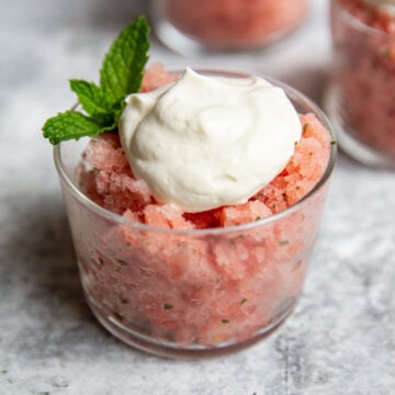 watermelon granita in a glass with a dollop of whipped cream and a sprig of mint