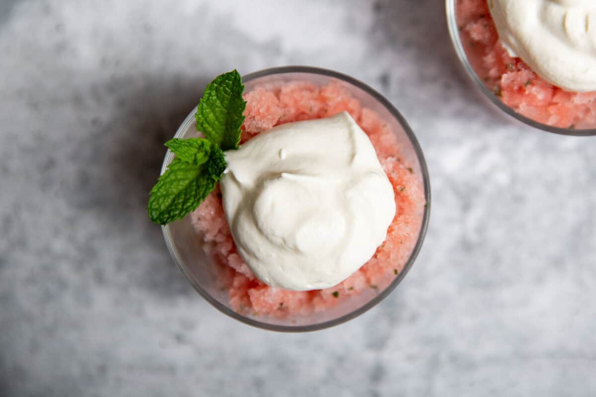 an overhead shot of a watermelon granita topped with whipped cream and a sprig of mint