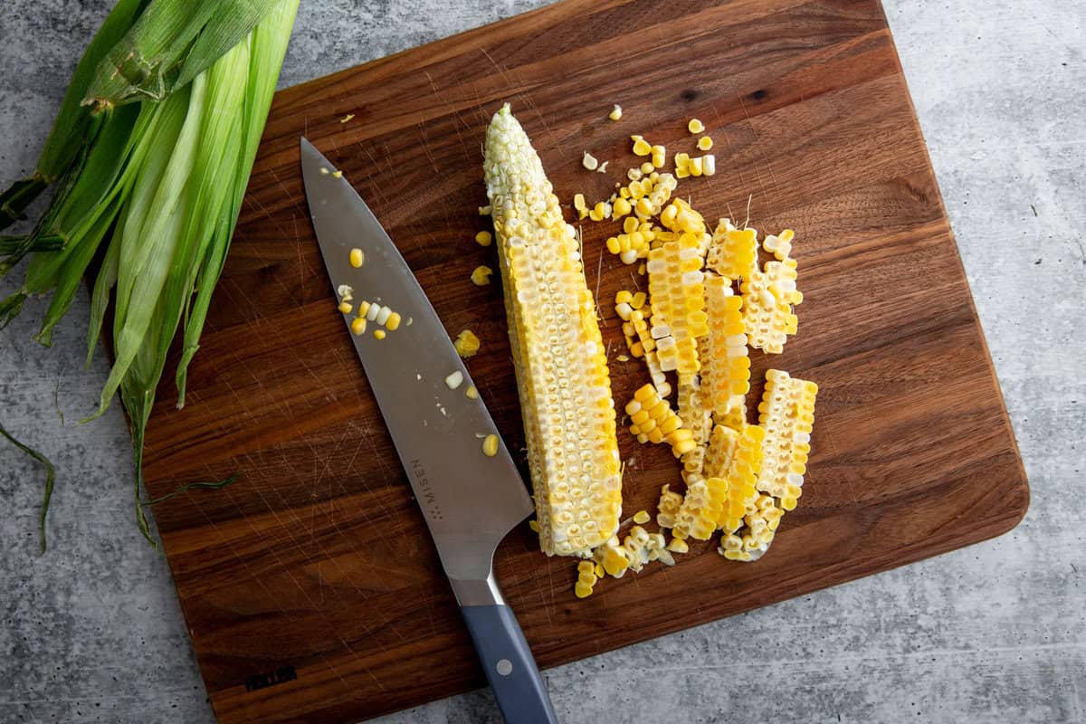 a cutting board with a knife and corn cob resting atop it