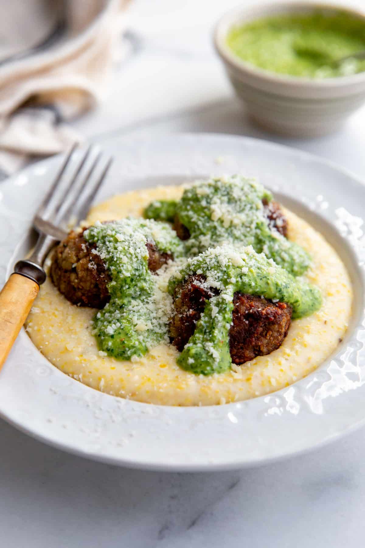 bison meatballs in a white bowl atop grits and topped with italian salsa verde