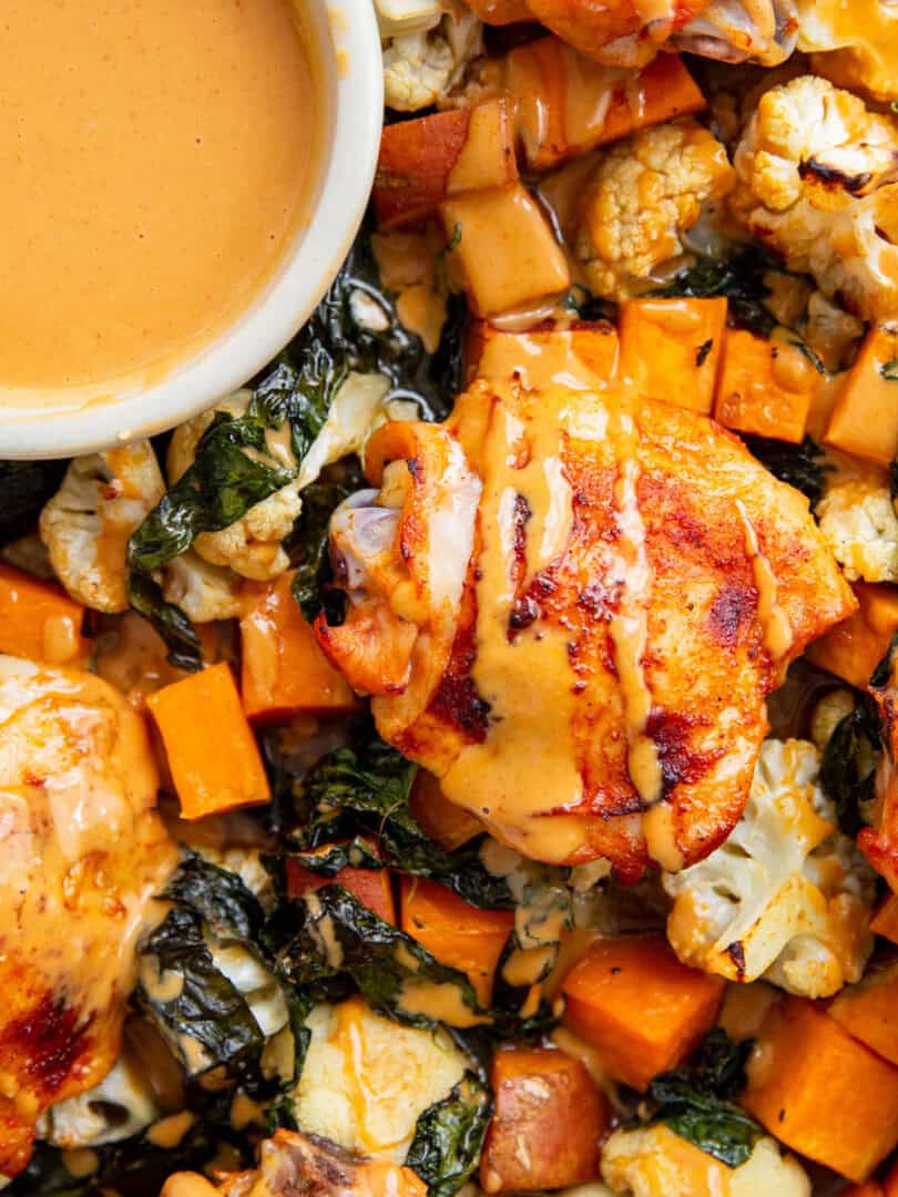 an overhead shot of gochujang chicken on a sheet pan with a bowl of sauce in the middle
