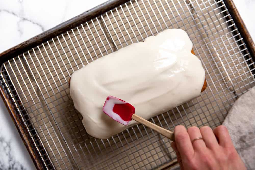 spreading a cream cheese glaze over a cake with a spatula 