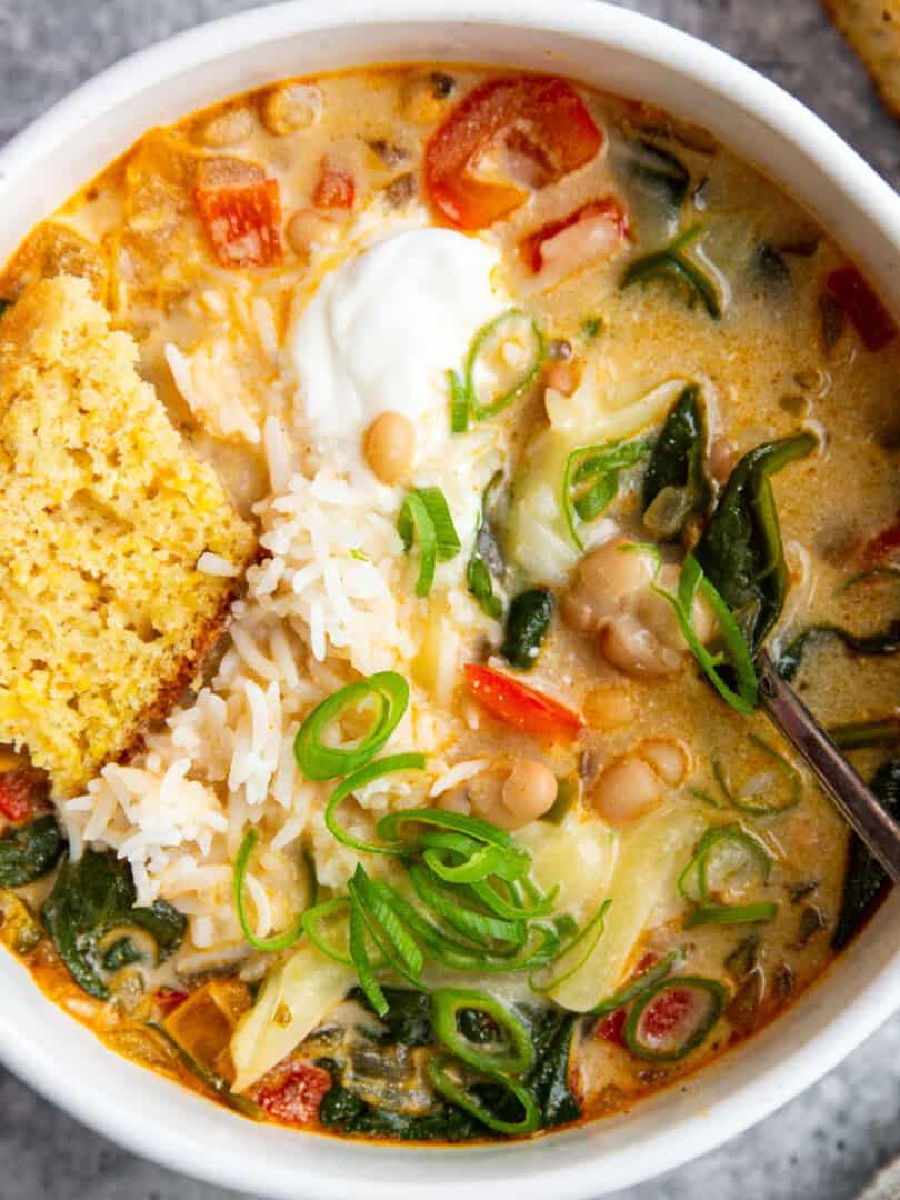 a bowl of creamy white bean soup topped with sour cream and cornbread.