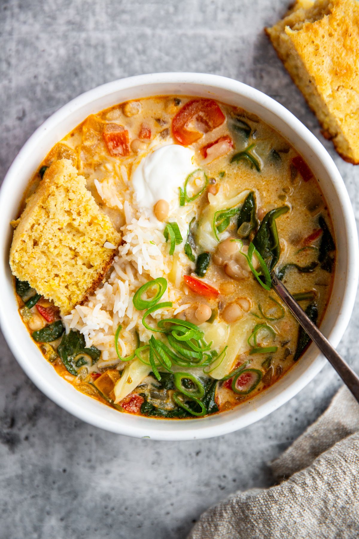 a bowl of creamy white bean soup topped with sour cream and cornbread.