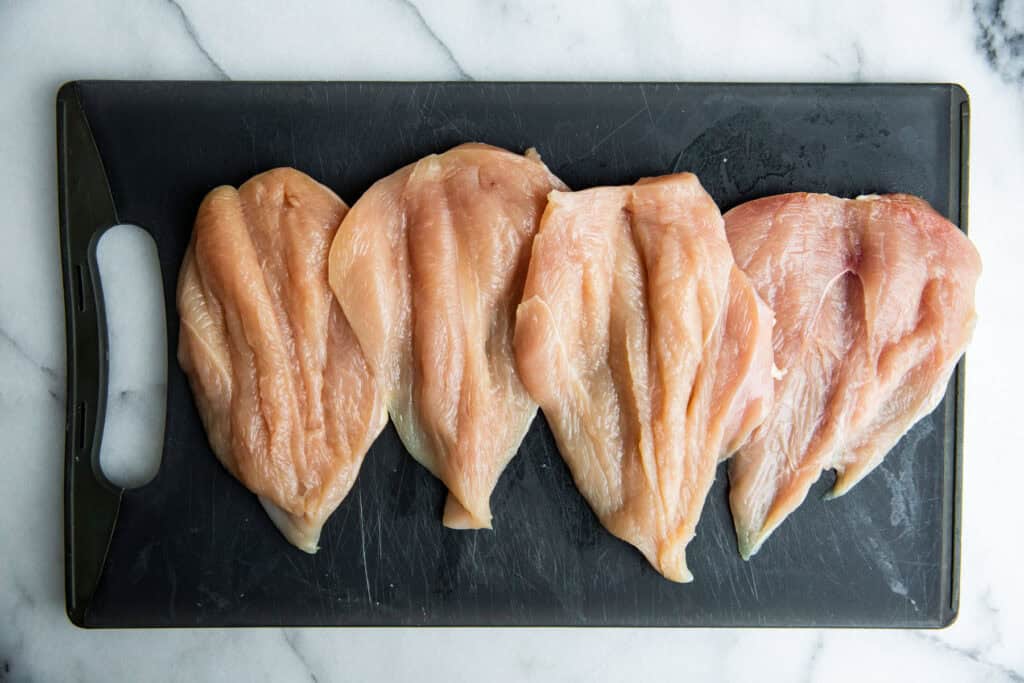 chicken breasts butterflied on a cutting board 