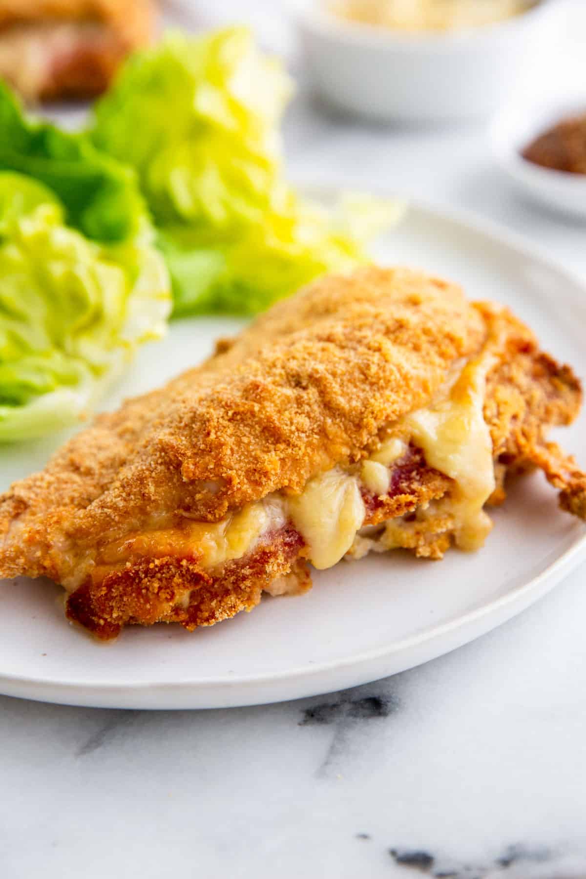 baked stuffed chicken on a white plate next to a salad 