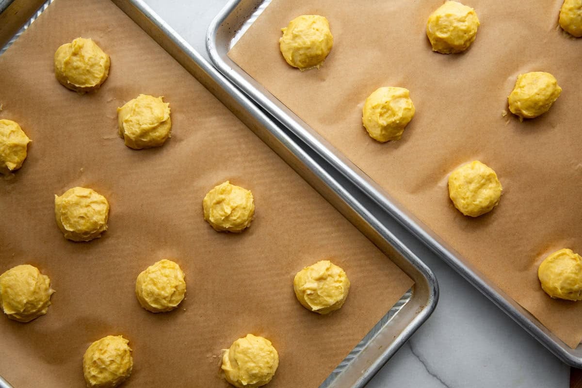 two baking sheets filled with cream puff shells 