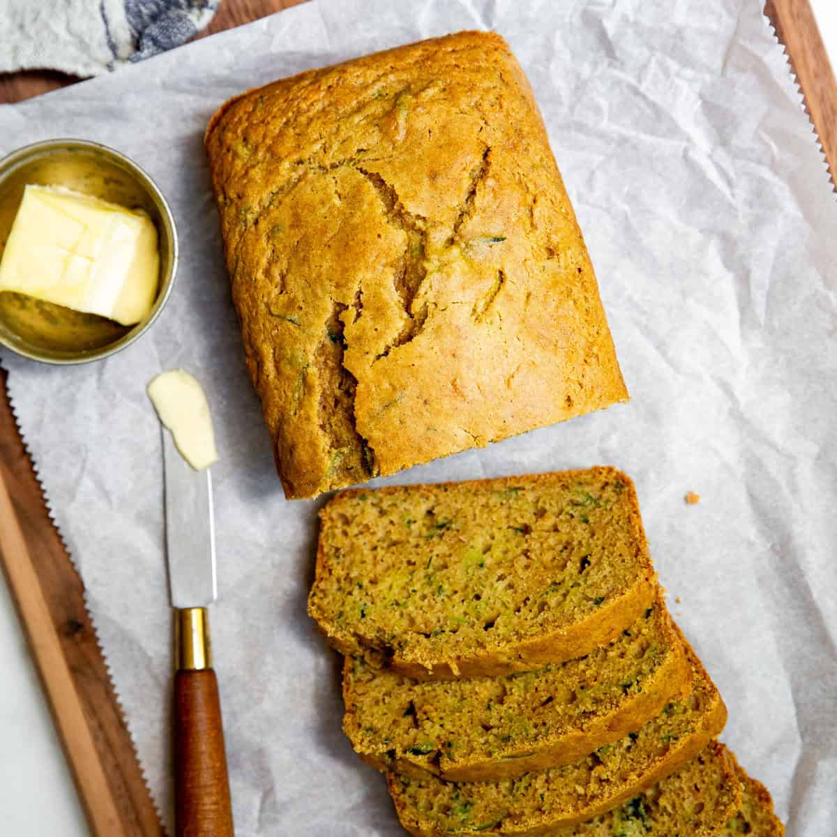 A loaf of gluten free bread partially sliced, sitting on a sheet of parchment paper.