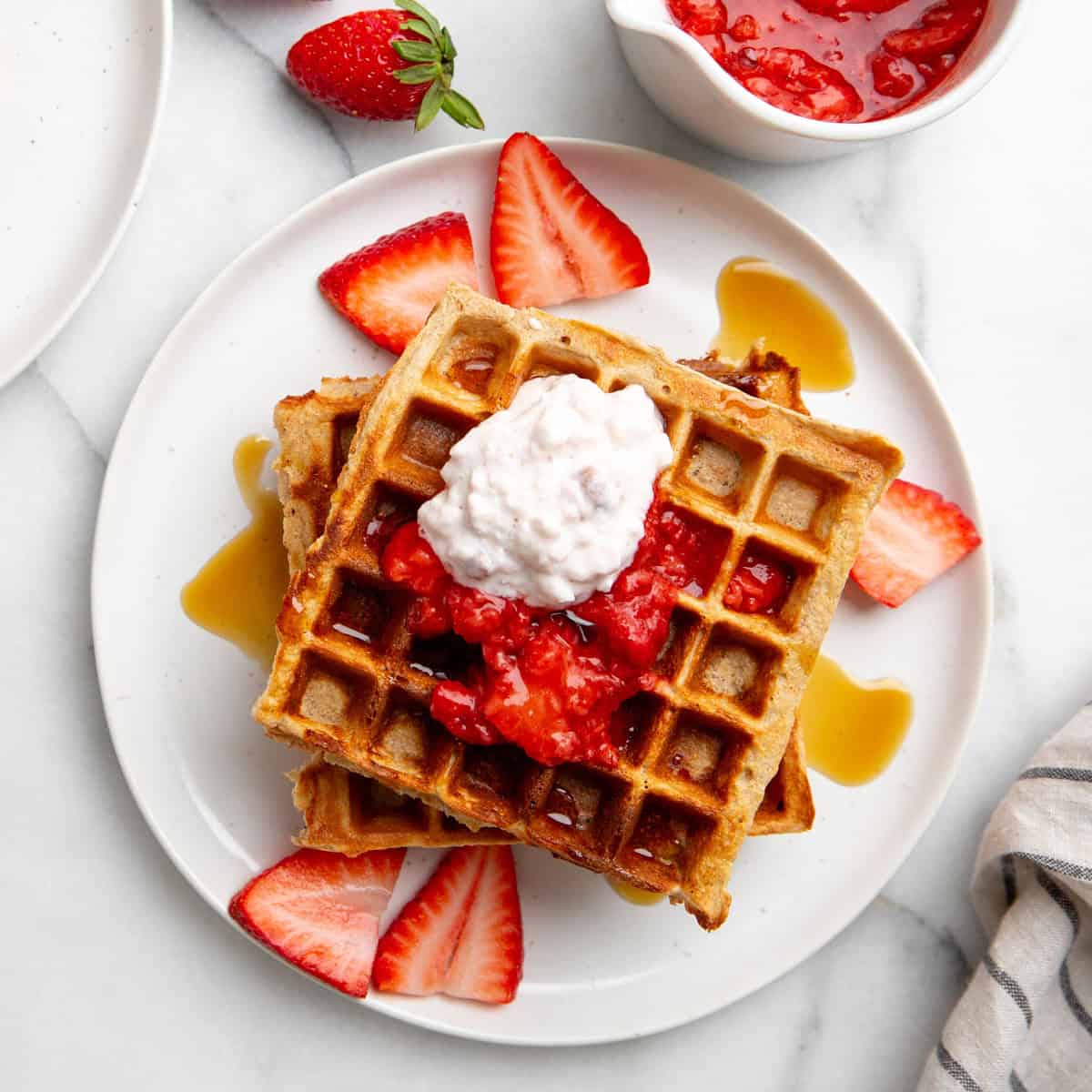 Gluten free breakfast waffles on a plate topped with strawberry slices and whipped cream.