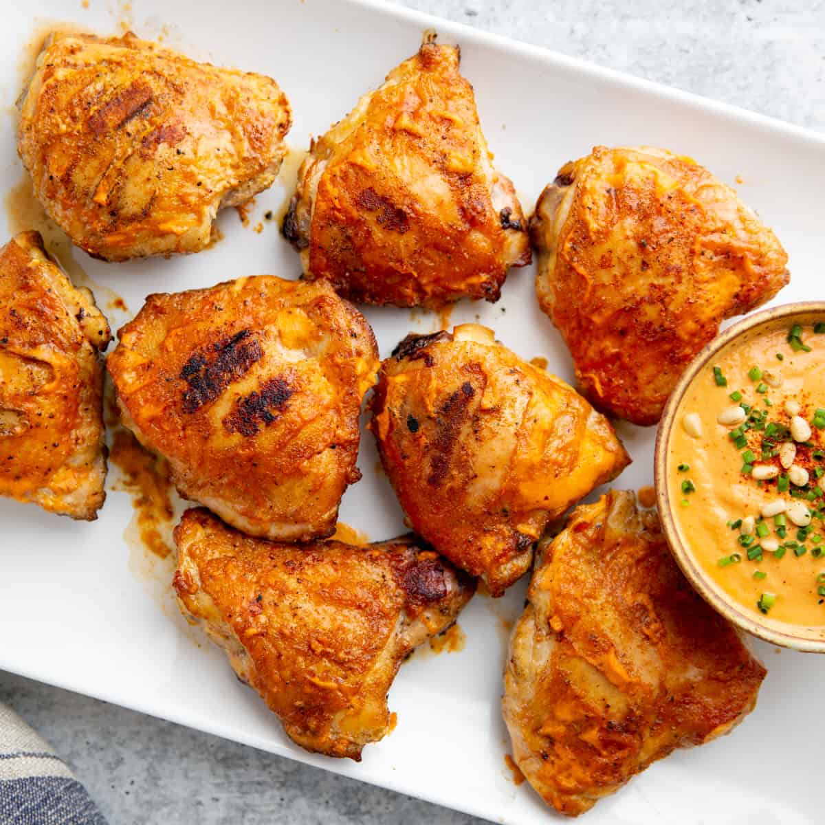 Eight pieces of healthy grilled bone-in chicken on a white serving platter with a bowl of creamy dipping sauce.