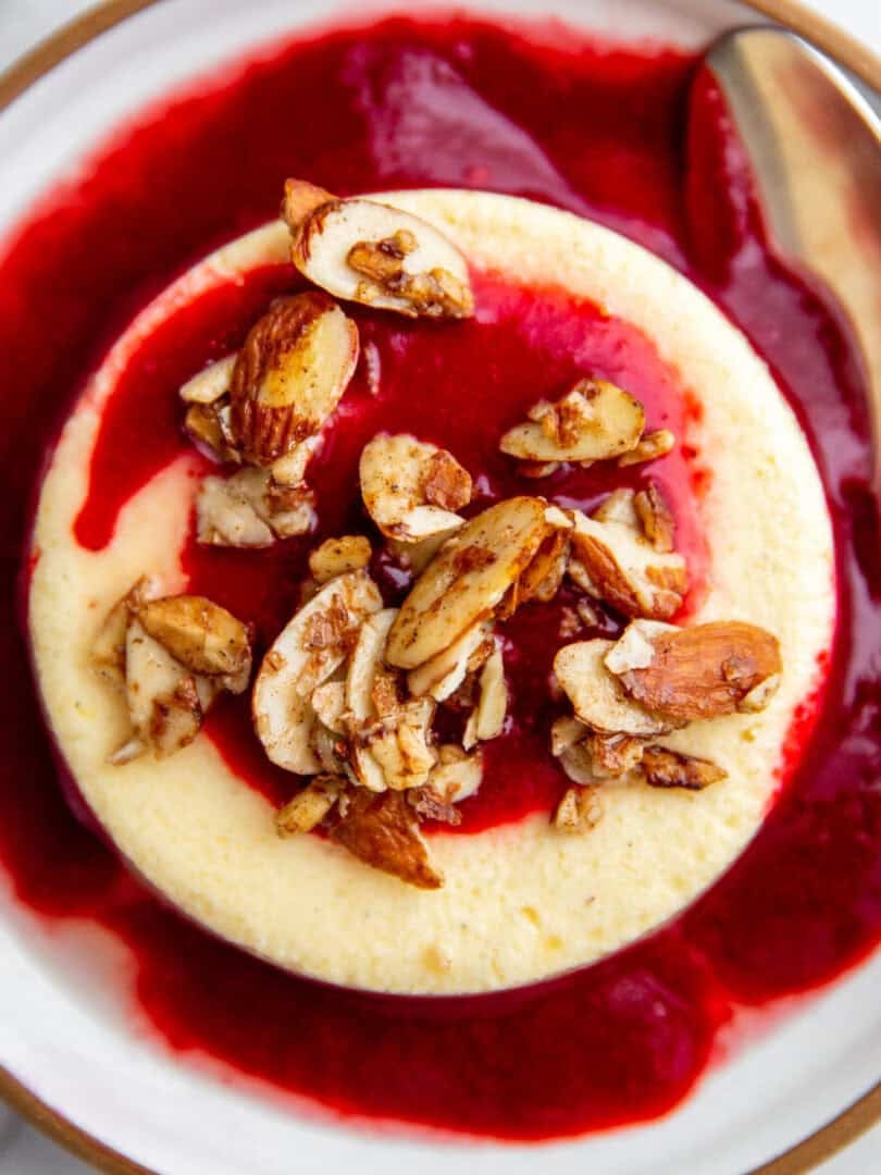 no crust mini cheesecakes topped with homamade strawberry sauce and maple almond clusters on a white plate