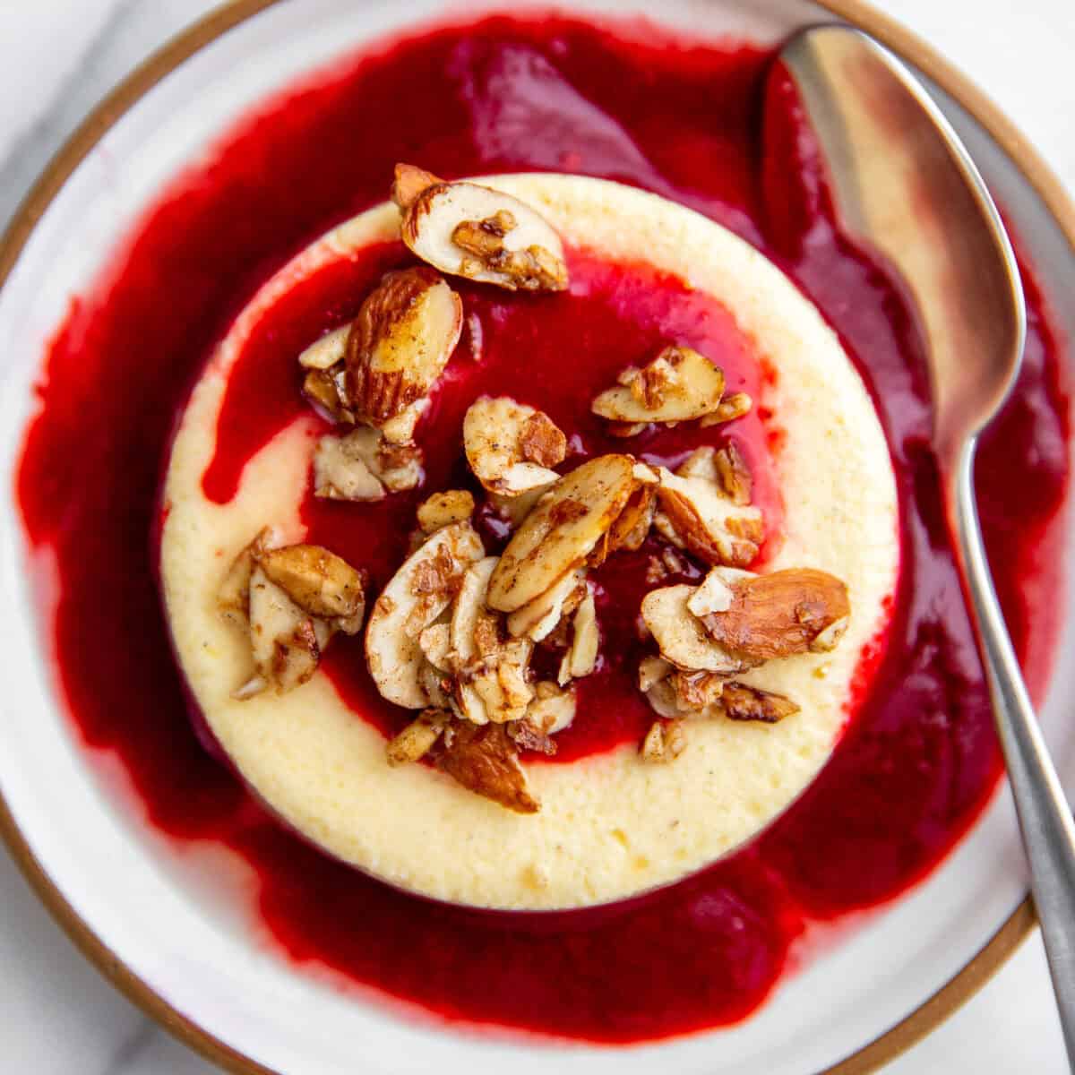 no crust mini cheesecakes topped with homamade strawberry sauce and maple almond clusters on a white plate