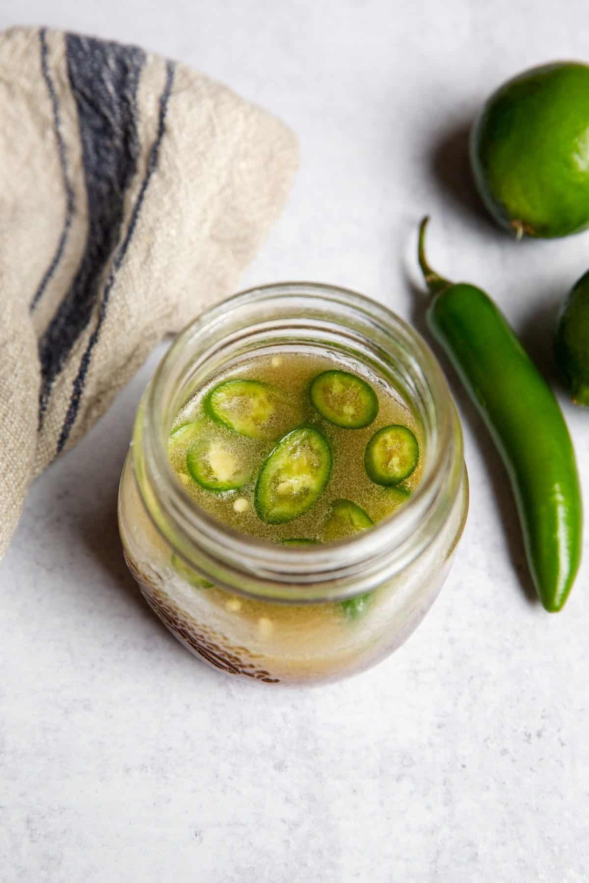 Jar of chili lime dressing on a counter with fresh limes and chiles