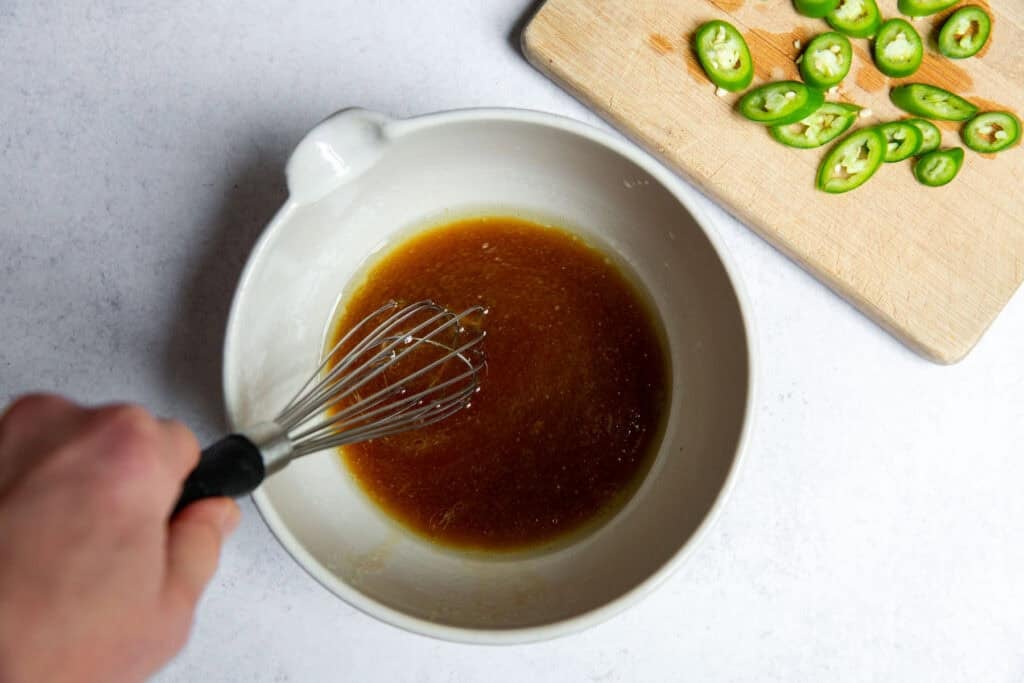 Grated garlic and lime juice in a glass mixing bowl with a whisk