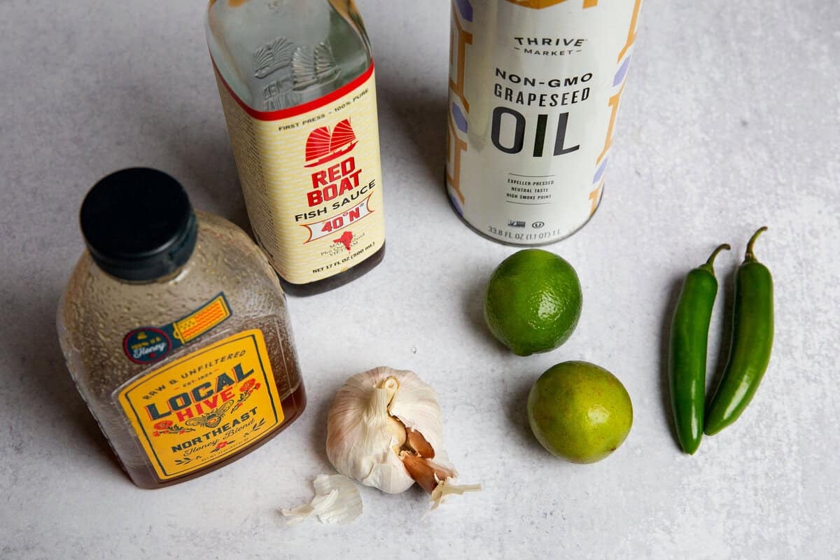 Chili lime dressing ingredients in small bowls: lime juice, honey, fish sauce, garlic, oil, and sliced chile