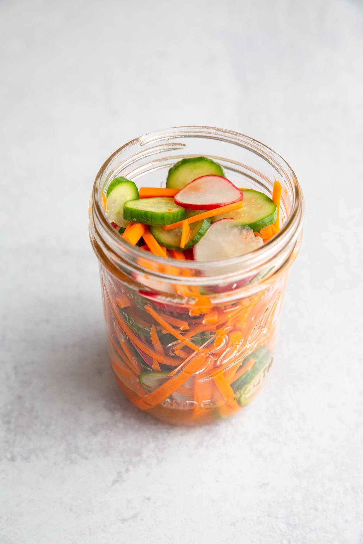 a mason jar filled with sliced veggies and topped with a vinegar mixture to pickle them.