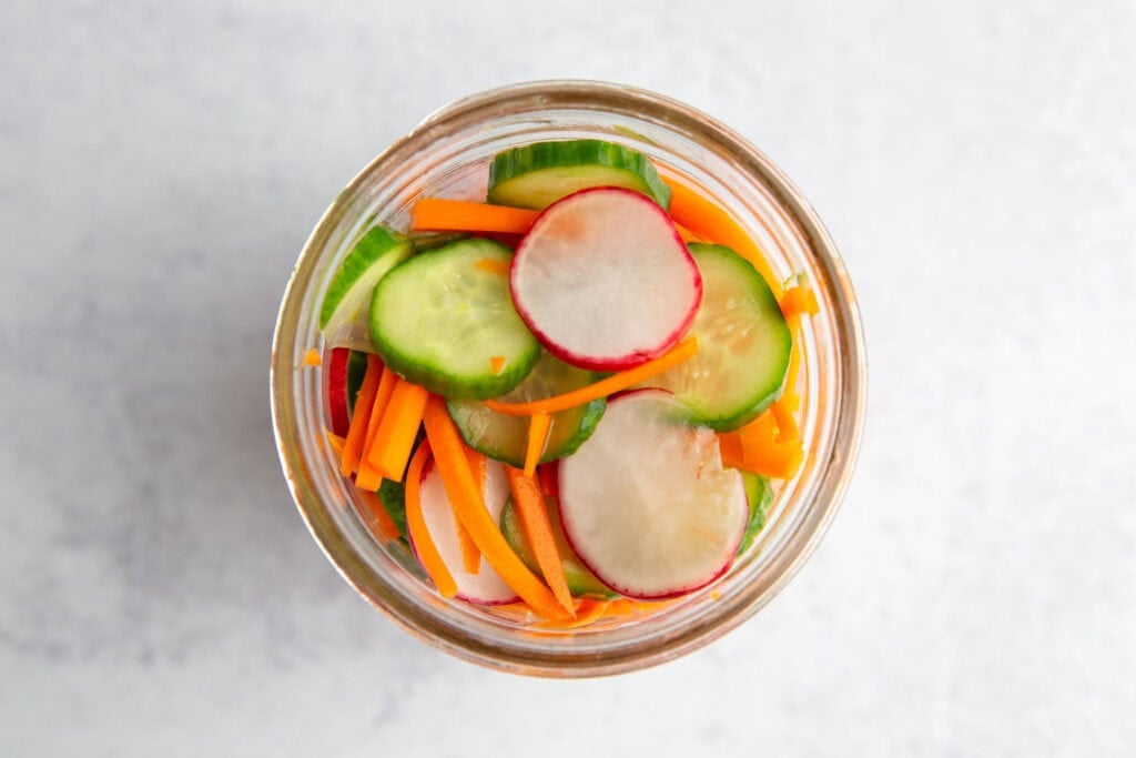 sliced carrots, cucumbers, and radishes in a mason jar after pickling.