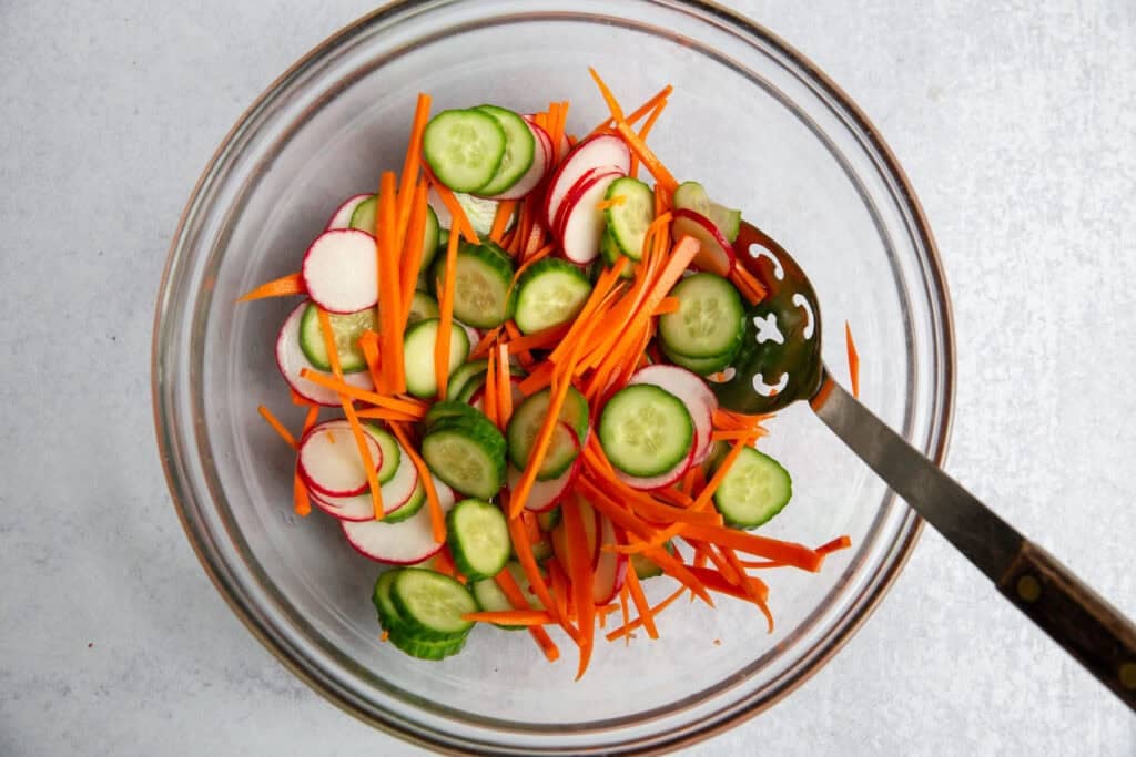 quick pickled vegetables in a glass bowl with a metal spoon.