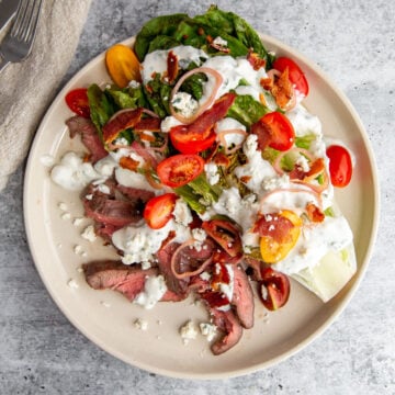 Grilled wedge steak salad with blue cheese, bacon, tomatoes, and pickled shallots on a white plate