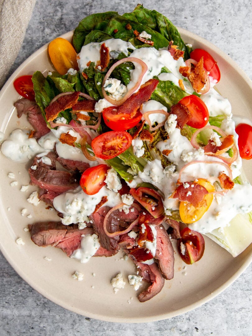 Grilled wedge steak salad with blue cheese, bacon, tomatoes, and pickled shallots on a white plate