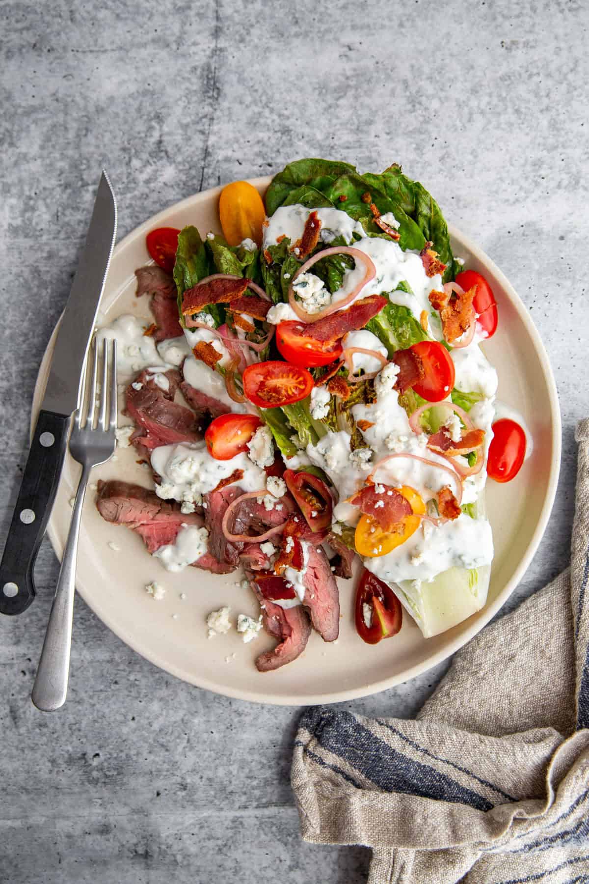 Grilled wedge steak salad with blue cheese, bacon, tomatoes, and pickled shallots on a white plate