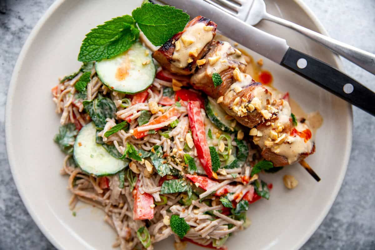 Close-up of grilled pork kebabs on skewers with fresh herbs and salad