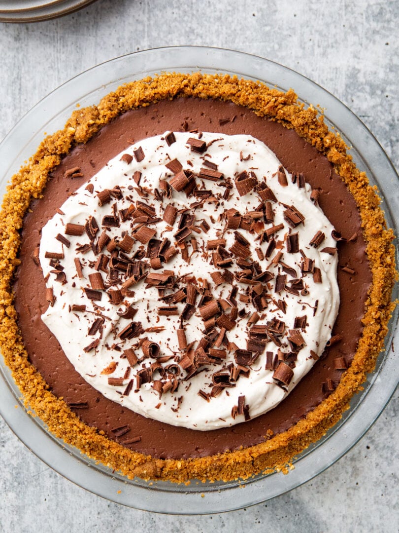 a chocolate pudding pie in a glass pie plate with whipped cream and chocolate shavings