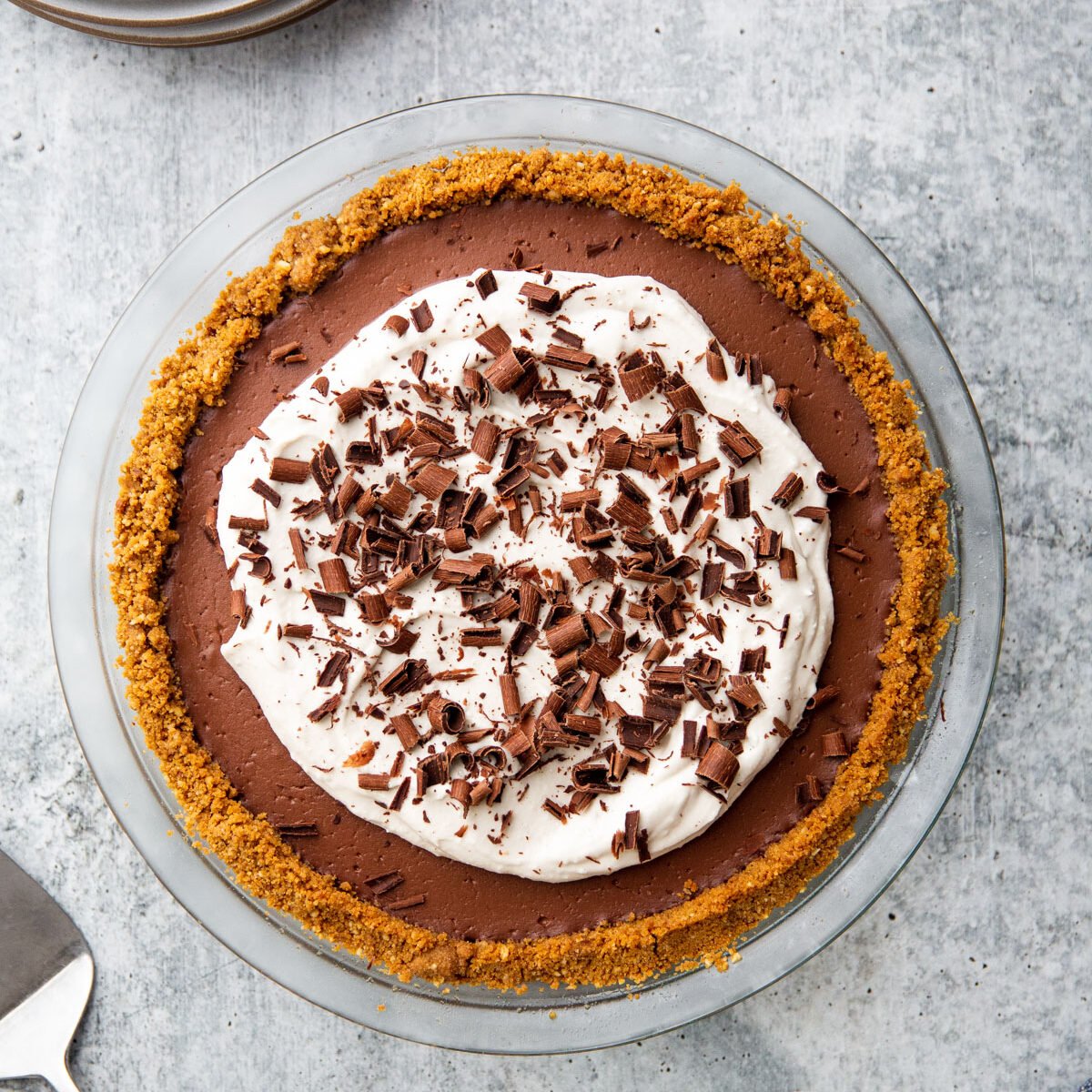 a chocolate pudding pie in a glass pie plate with whipped cream and chocolate shavings