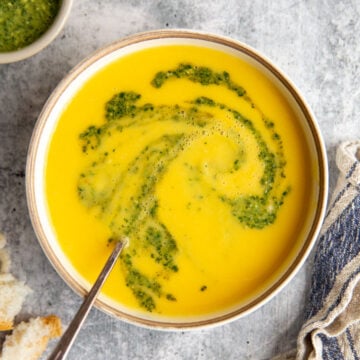 a bowl of cream yellow squash soup with a swirl of pesto on top.