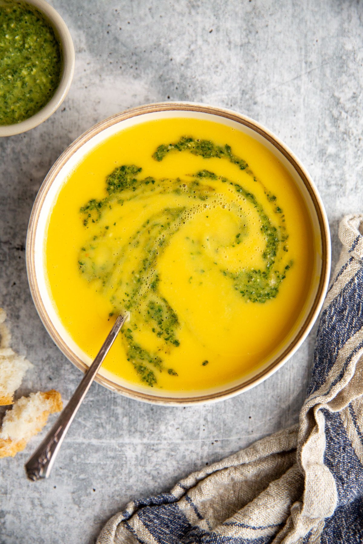 a bowl of cream yellow squash soup with a swirl of pesto on top.