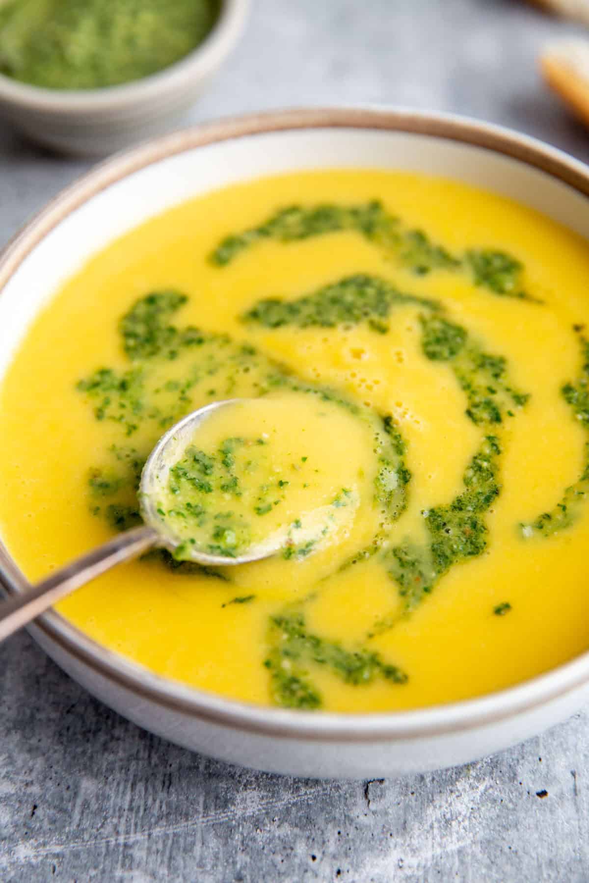 a spoon lifting a bite of yellow squash soup out of the bowl