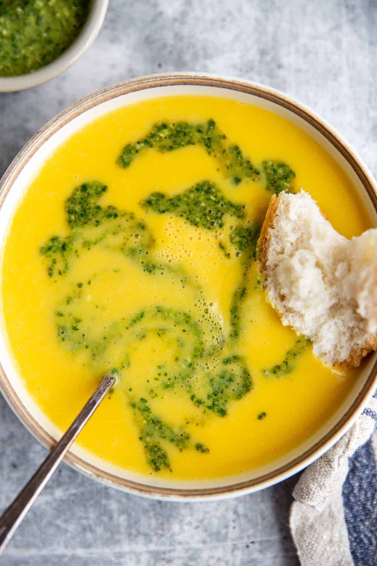serving a bowl of yellow squash soup with a piece of crusty bread