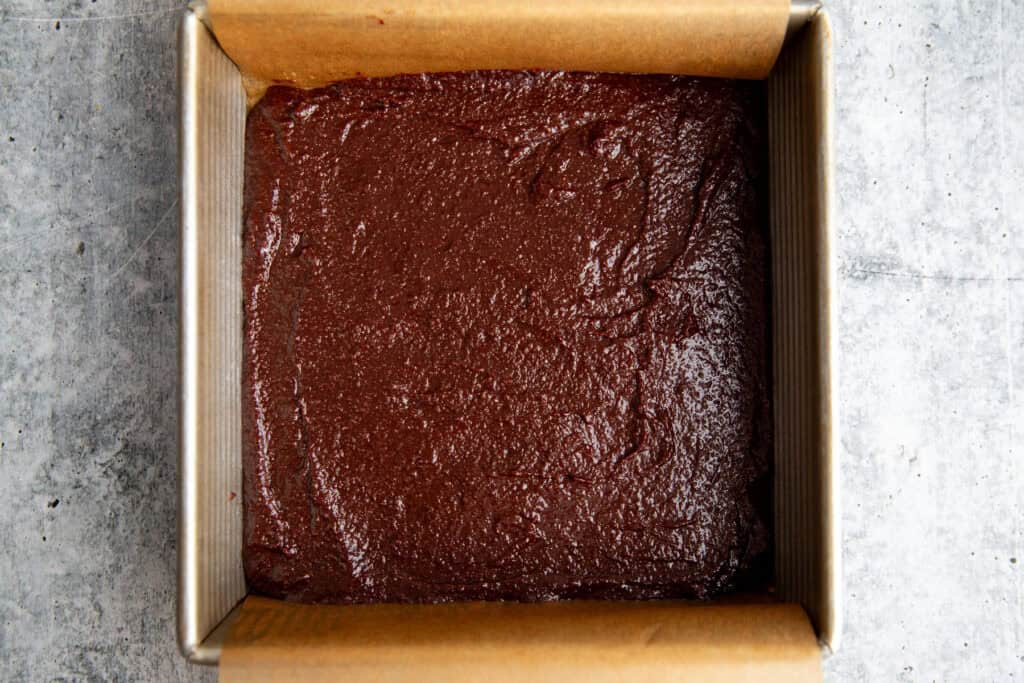 brownie batter spread into the bottom of a parchment lined square brownie pan