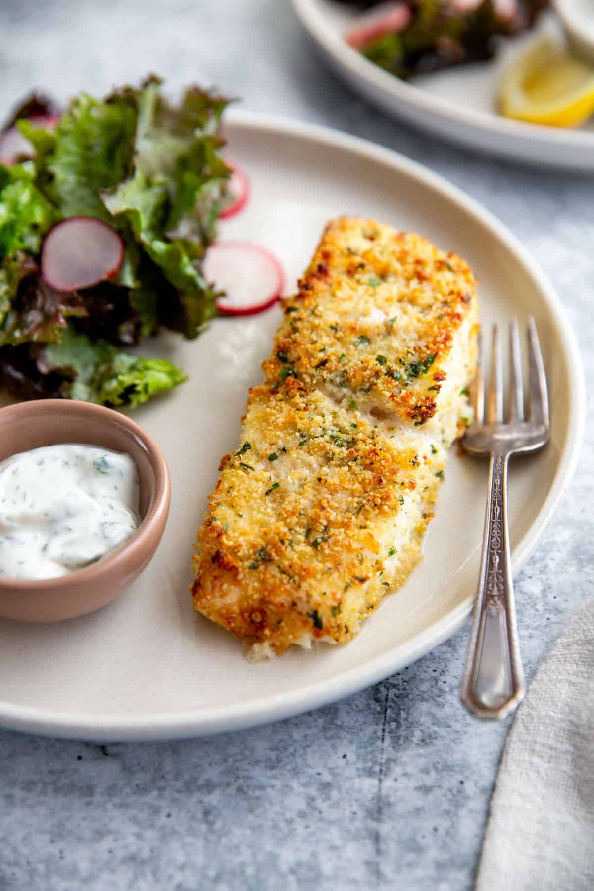 parmesan crusted halibut on a plate with a salad and dipping sauce.