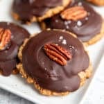 a tray of vegan turtles cookies set with a cookie base, caramel, hardened chocolate and a pecan on top