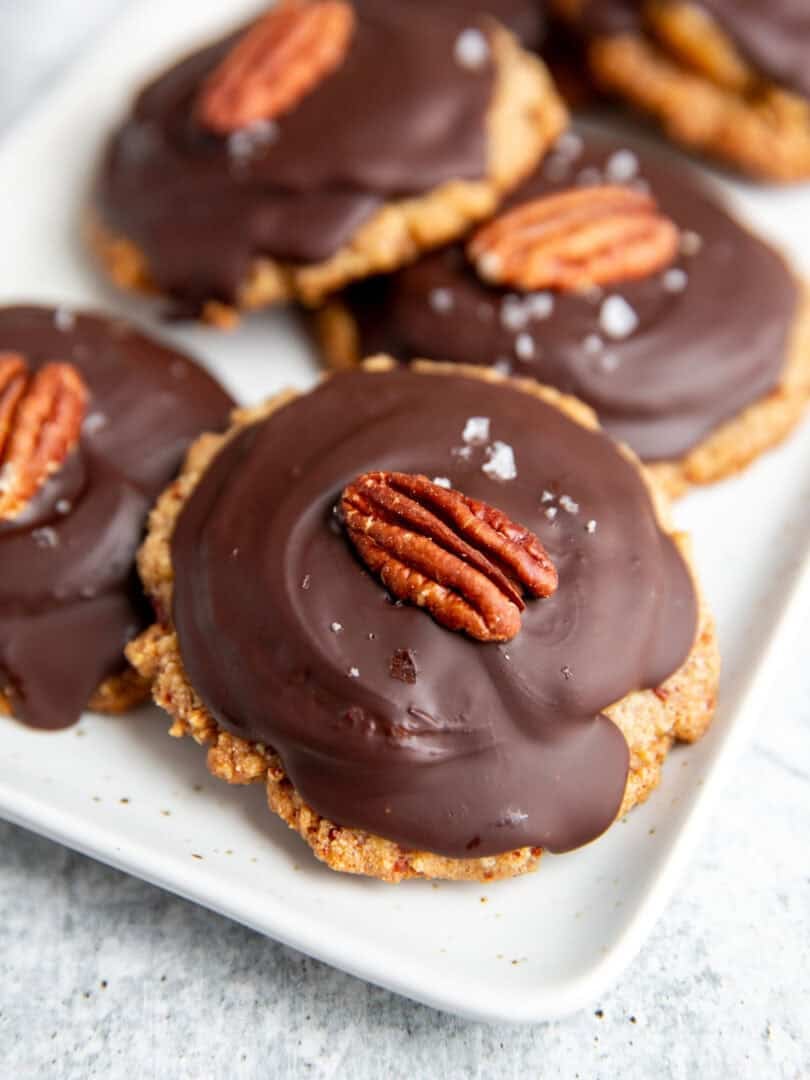 a tray of vegan turtles cookies set with a cookie base, caramel, hardened chocolate and a pecan on top