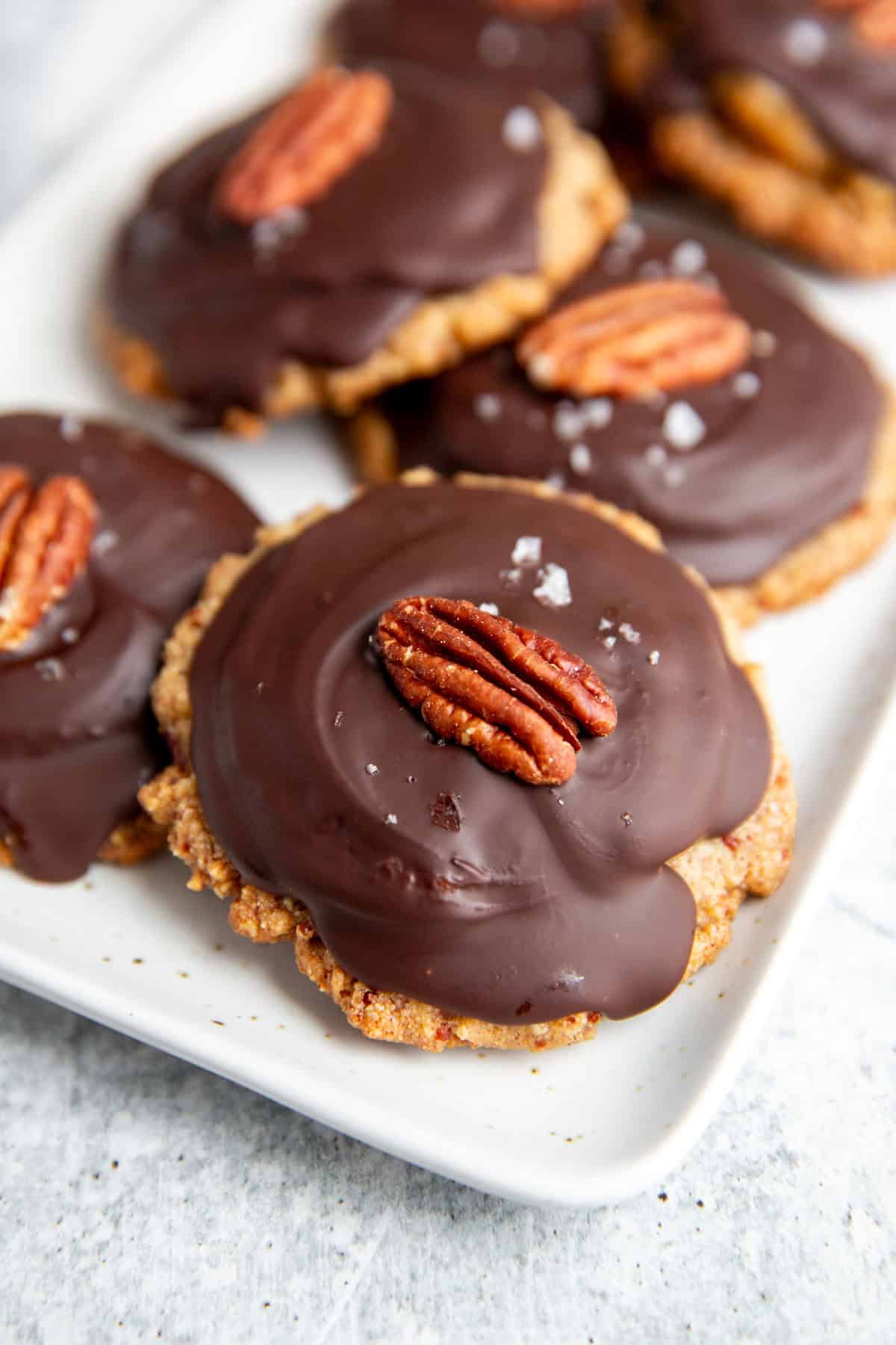 a tray of vegan turtles cookies set with a cookie base, caramel, hardened chocolate and a pecan on top