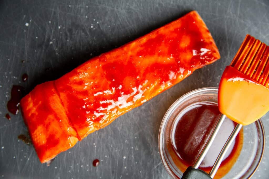 a piece of salmon resting on a pan with a bowl of glaze nearby