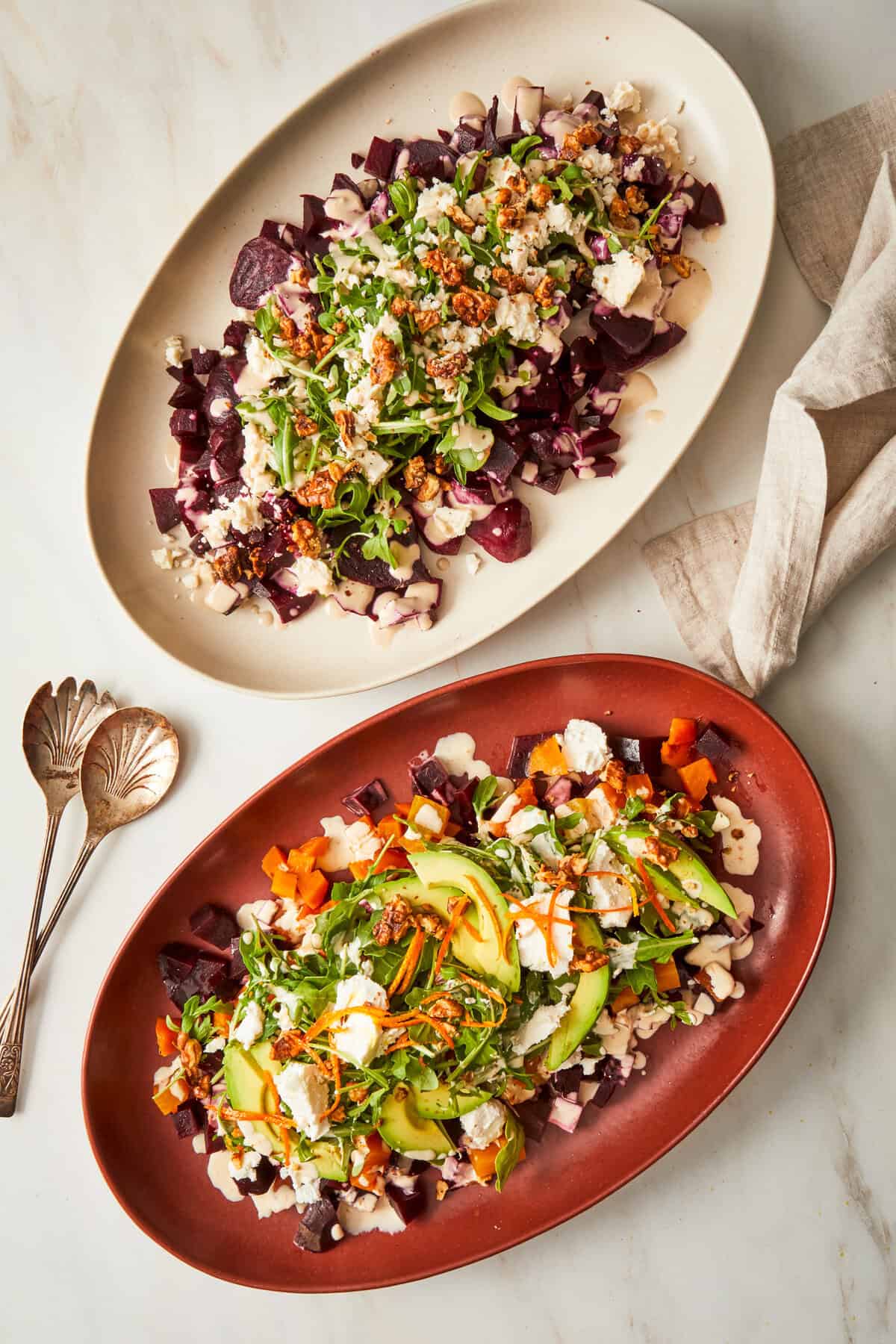 two roasted beet salads in serving trays finished with various toppings. 