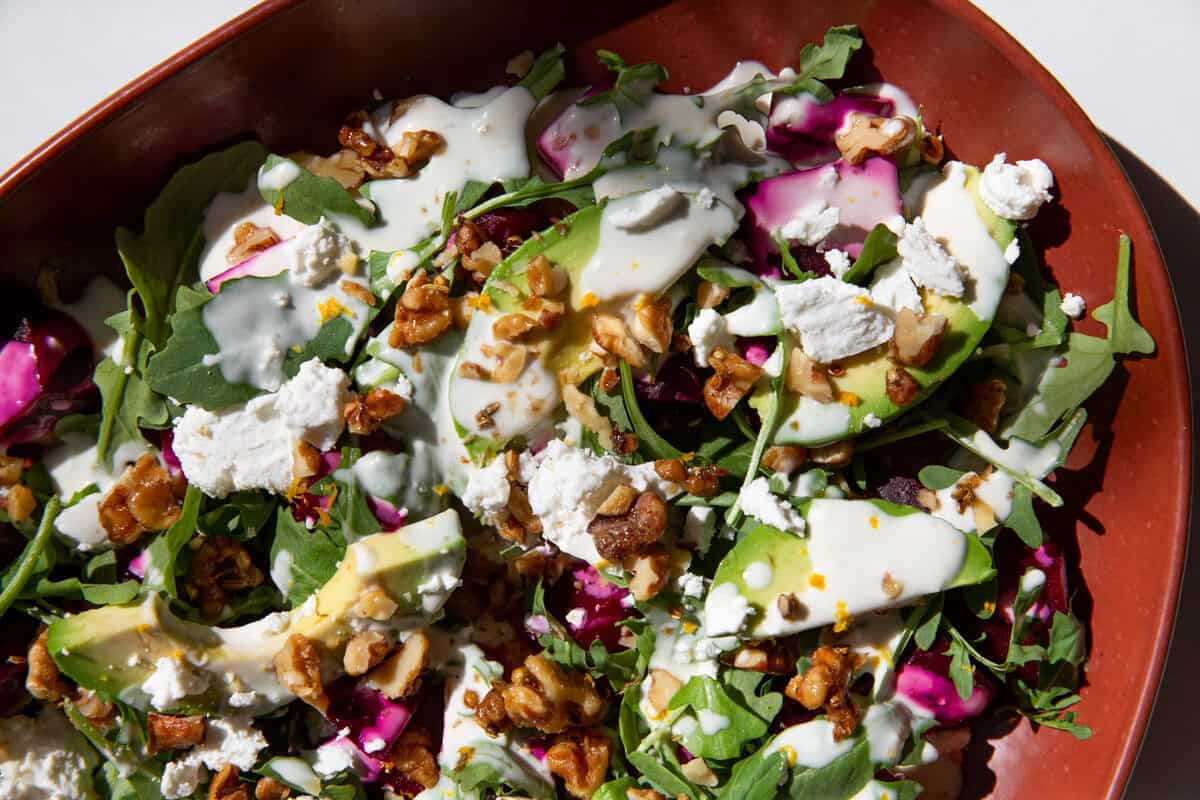 a close up of a roasted beet salad topped with creamy cheese, dressing, and chopped nuts